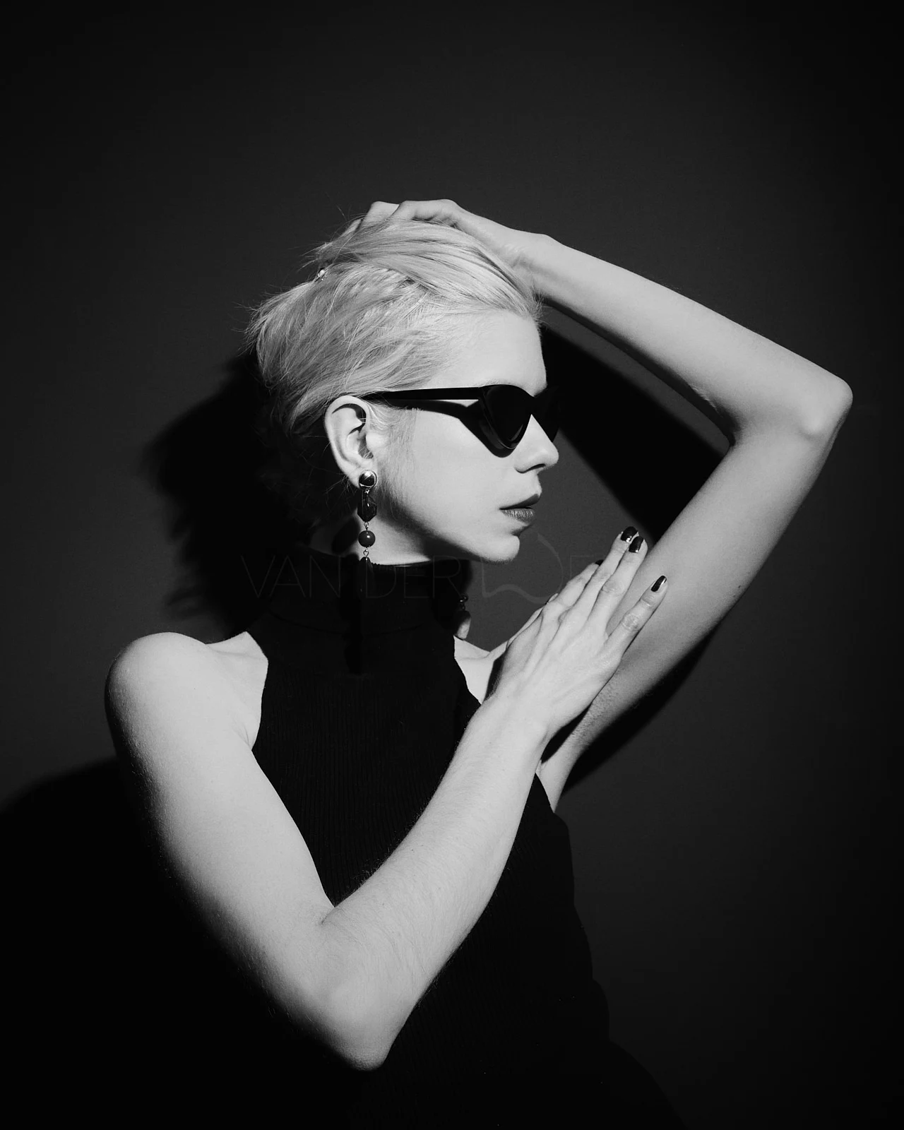 A woman in dark sunglasses with one arm curved above her head.